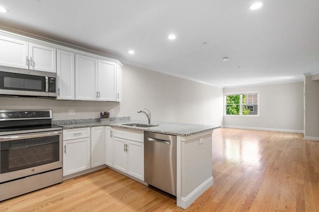 kitchen featuring light wood-style flooring, appliances with stainless steel finishes, open floor plan, a sink, and a peninsula