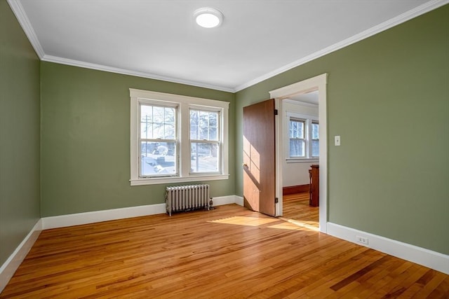 spare room with crown molding, baseboards, light wood-style flooring, and radiator