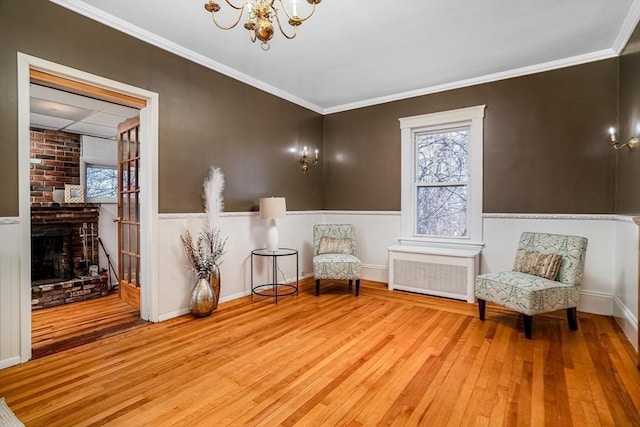 sitting room featuring radiator heating unit, an inviting chandelier, wood finished floors, and crown molding