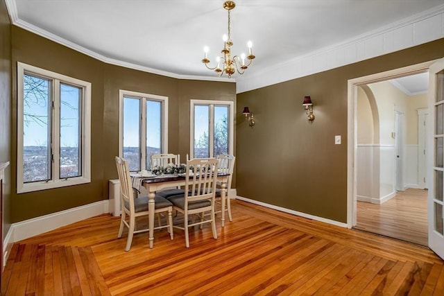 dining area featuring arched walkways, crown molding, light wood-style flooring, an inviting chandelier, and baseboards