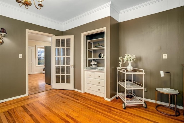 interior space featuring ornamental molding, light wood-type flooring, baseboards, and built in shelves