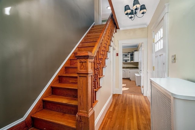 stairs with an inviting chandelier, crown molding, baseboards, and wood finished floors