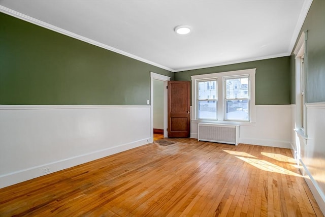 empty room featuring ornamental molding, radiator, a wainscoted wall, and light wood-style floors