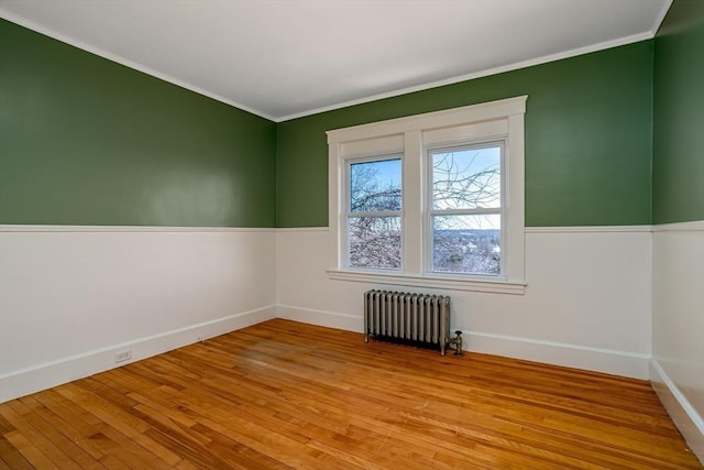 spare room with crown molding, radiator heating unit, baseboards, and light wood-style floors