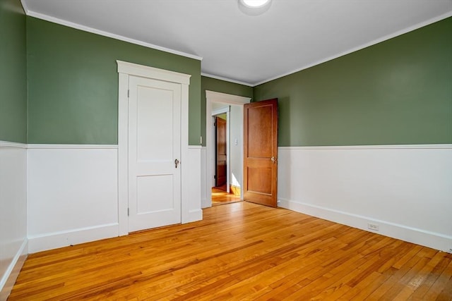 unfurnished room featuring wood-type flooring, crown molding, and wainscoting