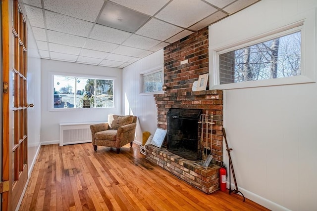 living area with hardwood / wood-style floors, radiator heating unit, a fireplace, and a drop ceiling