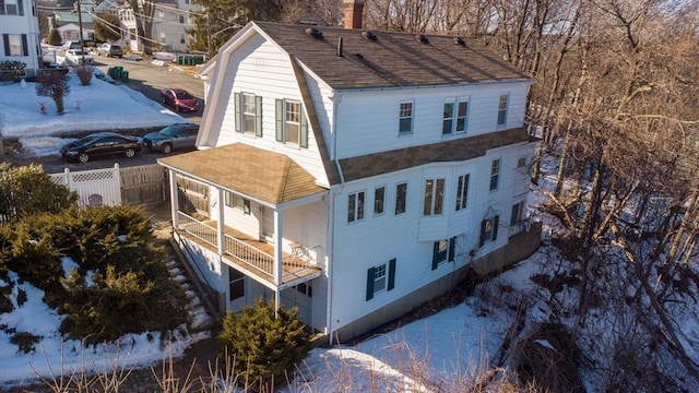 snow covered property featuring a shingled roof, a chimney, and fence