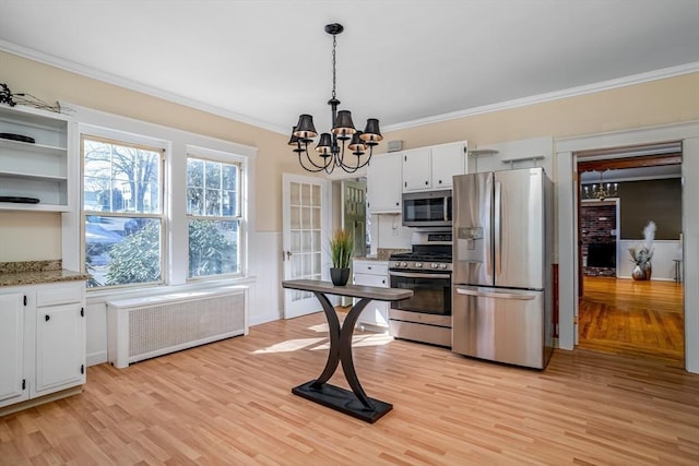 kitchen featuring white cabinets, appliances with stainless steel finishes, radiator, an inviting chandelier, and crown molding