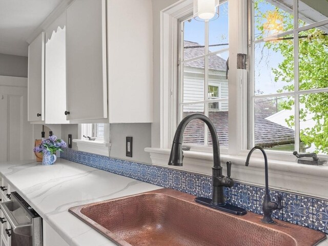 kitchen view of a sink, white cabinets, dishwasher, and light stone countertops