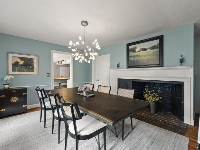 dining space with a fireplace with flush hearth, a chandelier, wood finished floors, and baseboards