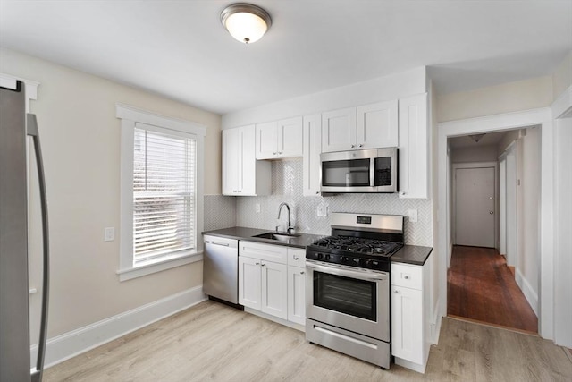 kitchen featuring dark countertops, light wood-style flooring, appliances with stainless steel finishes, a sink, and backsplash