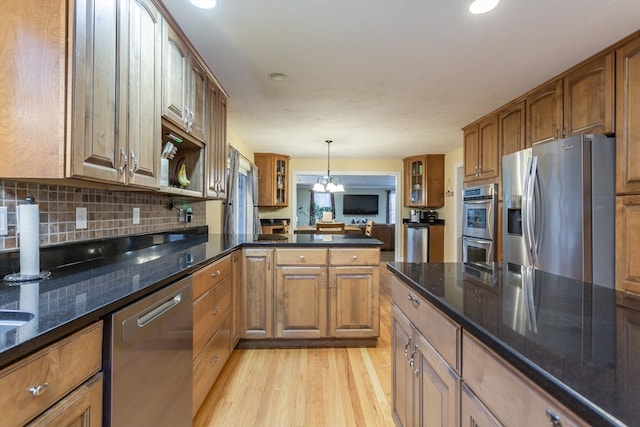 kitchen with dark stone counters, appliances with stainless steel finishes, light hardwood / wood-style flooring, backsplash, and decorative light fixtures