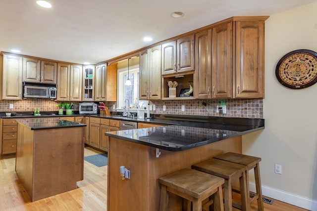 kitchen featuring kitchen peninsula, light hardwood / wood-style flooring, stainless steel appliances, tasteful backsplash, and a center island