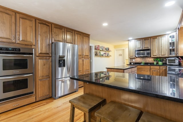 kitchen with appliances with stainless steel finishes, light hardwood / wood-style floors, dark stone countertops, tasteful backsplash, and a breakfast bar area