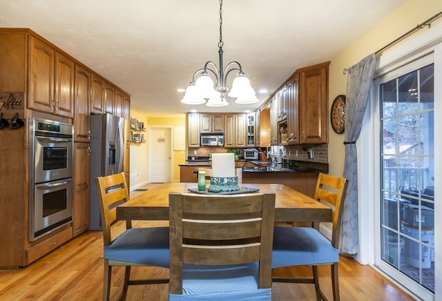 kitchen featuring pendant lighting, backsplash, light hardwood / wood-style floors, stainless steel appliances, and an inviting chandelier