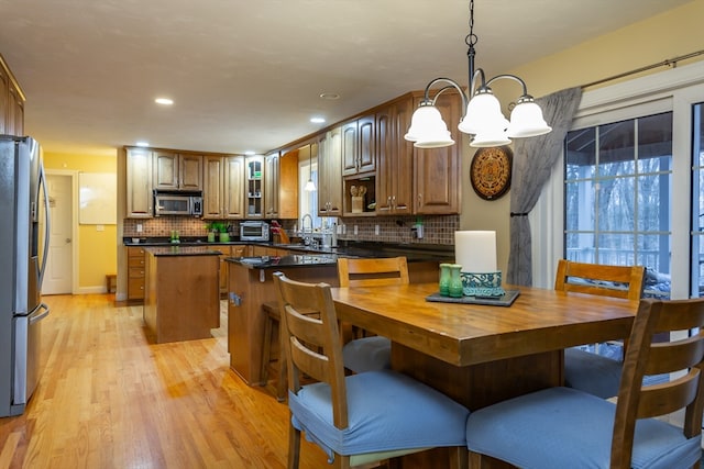 kitchen featuring appliances with stainless steel finishes, light wood-type flooring, a chandelier, tasteful backsplash, and pendant lighting