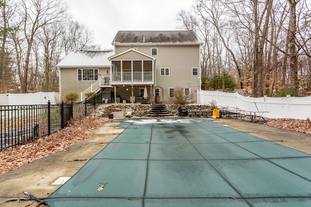 back of property with a sunroom, a covered pool, and a patio area