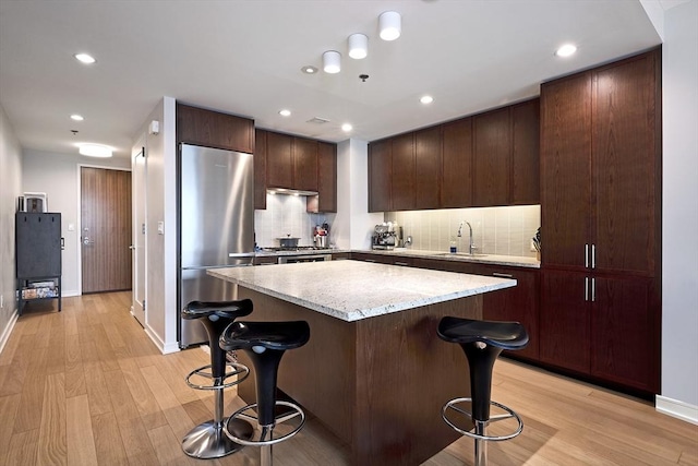 580 Washington St Unit 10A, Boston, MA 02111 - kitchen with freestanding refrigerator, a breakfast bar, a center island, light wood-style flooring, and backsplash
