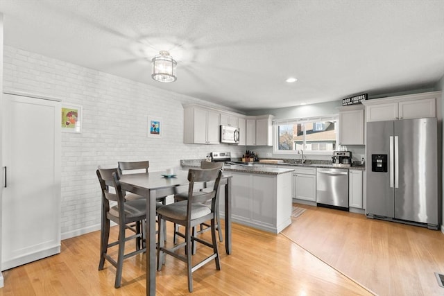 kitchen with sink, stainless steel appliances, brick wall, and light hardwood / wood-style floors