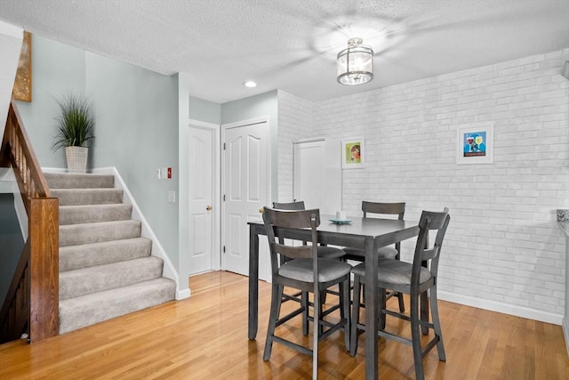 dining room with hardwood / wood-style flooring, a textured ceiling, and brick wall