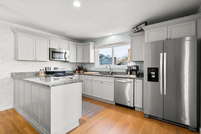 kitchen with white cabinets, sink, light wood-type flooring, kitchen peninsula, and stainless steel appliances