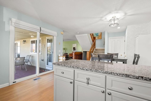 kitchen with white cabinets, light wood-type flooring, and light stone counters