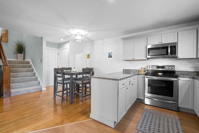 kitchen featuring kitchen peninsula, appliances with stainless steel finishes, light hardwood / wood-style floors, and dark stone countertops