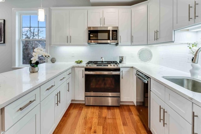 kitchen with appliances with stainless steel finishes, decorative light fixtures, white cabinetry, sink, and light hardwood / wood-style flooring