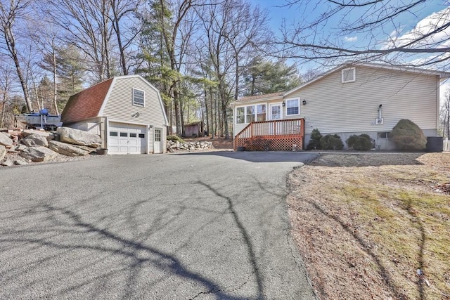 view of side of home with a wooden deck, a gambrel roof, an outdoor structure, a garage, and aphalt driveway