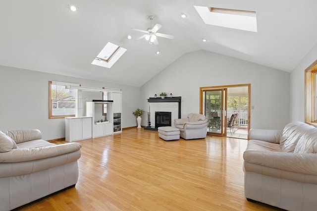 living area with a skylight, ceiling fan, light wood-style flooring, and a fireplace