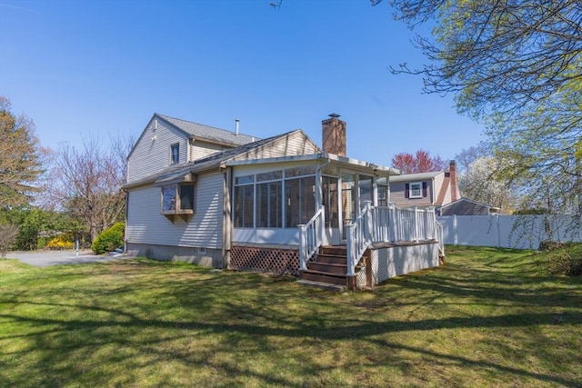 back of property featuring fence, a chimney, a yard, and a sunroom