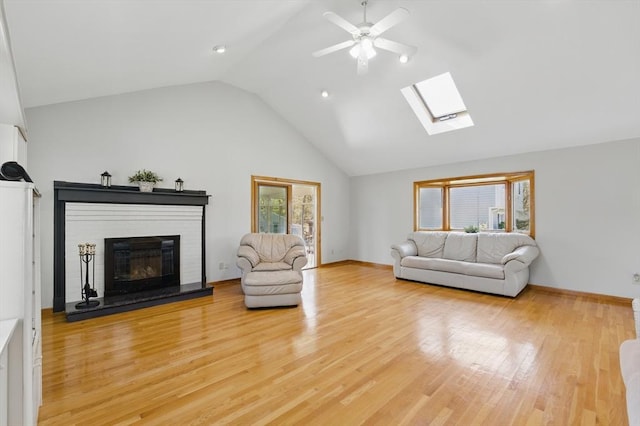 living room with a fireplace, high vaulted ceiling, light wood-type flooring, a ceiling fan, and a skylight