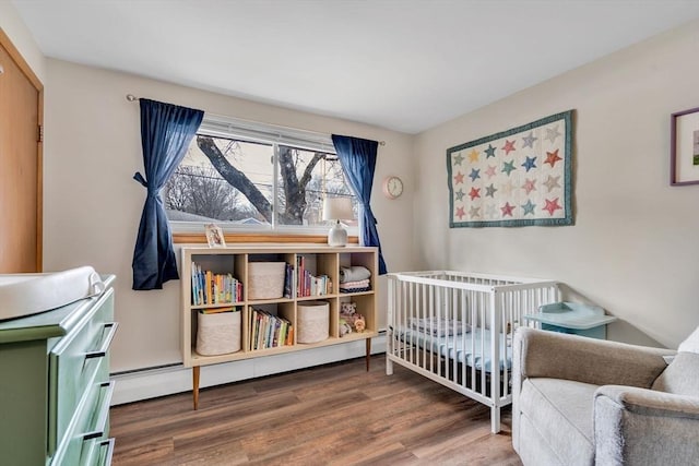 bedroom featuring a crib, a baseboard radiator, and wood finished floors