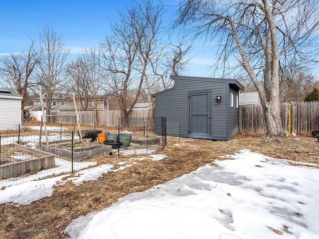 snowy yard featuring a garden, an outdoor structure, a shed, and fence