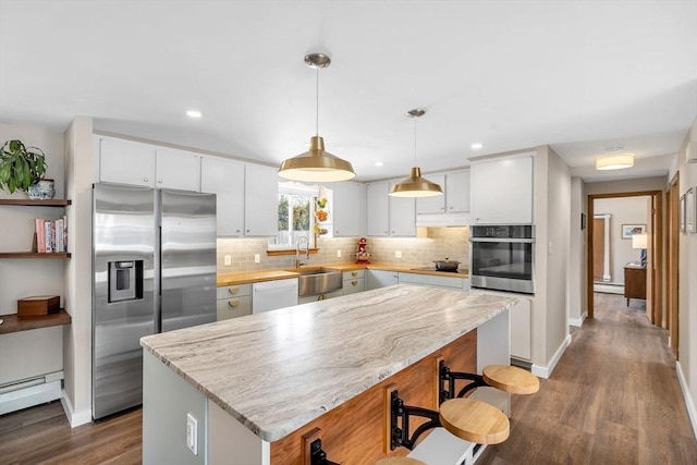 kitchen featuring stainless steel appliances, a sink, baseboard heating, decorative backsplash, and a center island