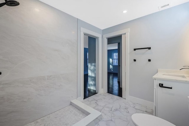 bathroom with a tile shower, vanity, and toilet