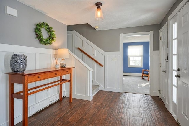 foyer entrance with stairway, a baseboard radiator, dark wood finished floors, and a decorative wall