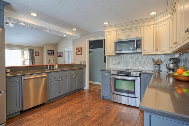 kitchen with dark countertops, a peninsula, appliances with stainless steel finishes, and a sink