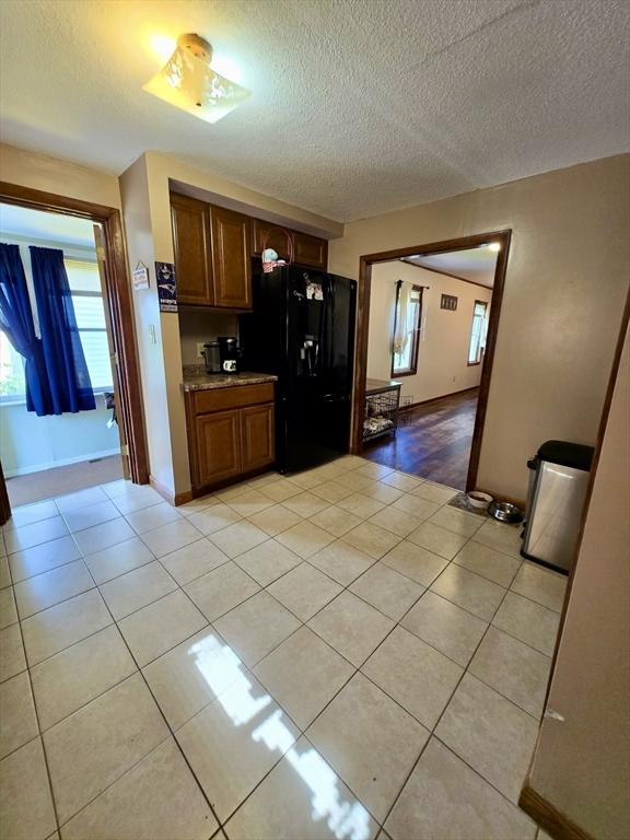 kitchen featuring black fridge, a textured ceiling, light tile patterned flooring, brown cabinets, and light countertops