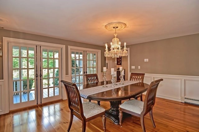 dining area with french doors, a chandelier, wood finished floors, a decorative wall, and wainscoting