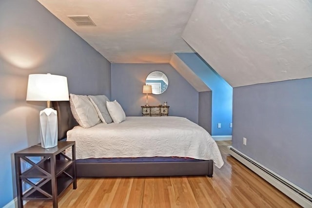 bedroom with baseboard heating, vaulted ceiling, and wood finished floors
