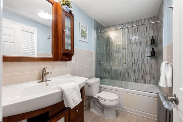 bathroom with toilet, shower / bath combination with glass door, vanity, tile walls, and radiator