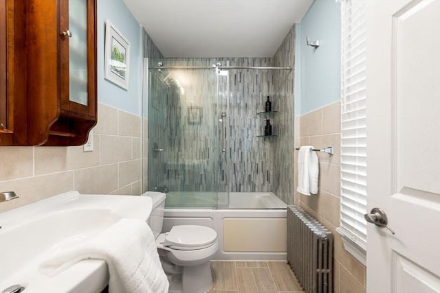 bathroom with toilet, bath / shower combo with glass door, radiator heating unit, and tile walls