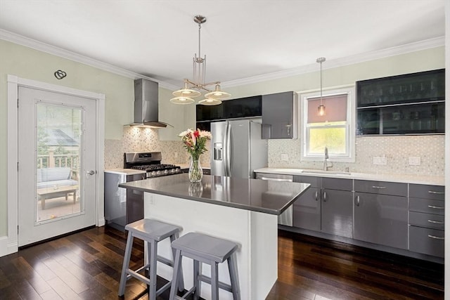 kitchen featuring a kitchen island, a sink, appliances with stainless steel finishes, wall chimney exhaust hood, and pendant lighting