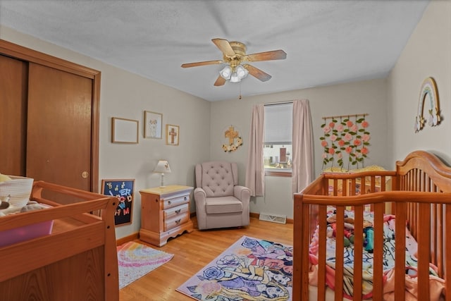 bedroom with ceiling fan, a textured ceiling, a closet, a nursery area, and light wood-type flooring