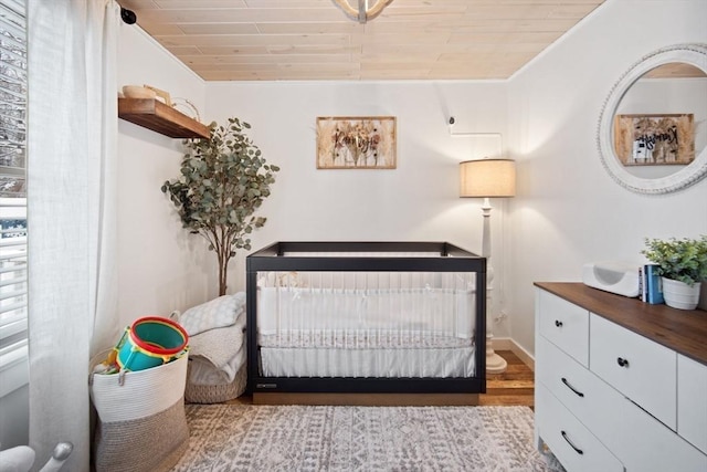 bedroom featuring wooden ceiling, light hardwood / wood-style flooring, ornamental molding, and a crib