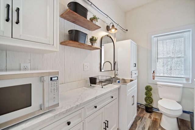 interior space with hardwood / wood-style floors, sink, white cabinets, and light stone countertops