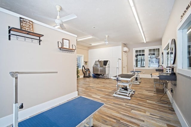 workout room with light wood-type flooring, ceiling fan, and a wall unit AC