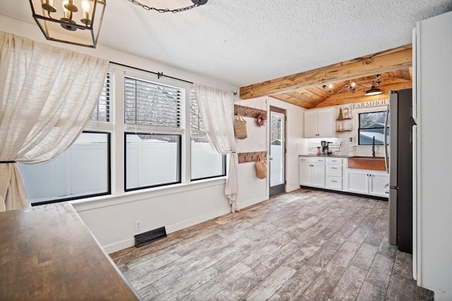 kitchen with a textured ceiling, white cabinets, vaulted ceiling with beams, decorative backsplash, and light hardwood / wood-style flooring