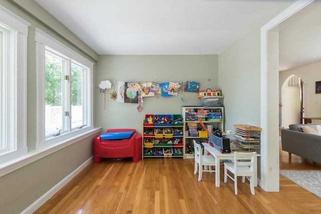 recreation room featuring wood finished floors, arched walkways, and baseboards